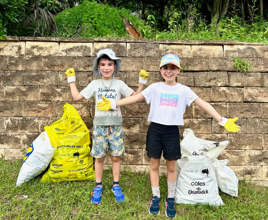 Two children with bright yellow gardening gloves proudly posing next to full rubbish bags.
